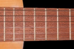 Fragment of the fingerboard with frets of old traditional wooden acoustic guitar with six strings, top view close-up on a black background 