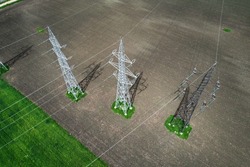 Aerial view of high voltage electric power transmission towers with power lines running across agriculture fields in rural area