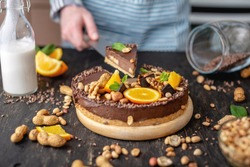 Pastry chef in hand holding a piece of chocolate cake with orange, mint leaves, peanuts and nuts. Concept healthy raw gluten-free and milk-and flour-free desserts for vegan food