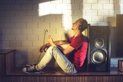 Handsome man, a music lover listens to music with headphones with a mobile phone in a modern interior against the media and large speakers. Enjoying music is fun and communicates on Internet at home