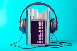 Phone with black headphones with a stack of books on a blue background. The concept of audio books and modern education