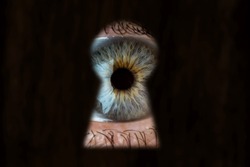Female blue eye looking through the keyhole. The concept of voyeurism, curiosity, Stalker, surveillance and security