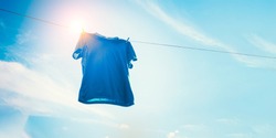 Blue t-shirt on clothes line against sun and blue sky with clouds.
