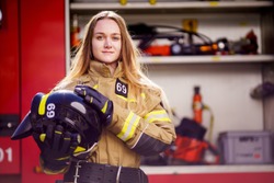 Photo of woman firefighter with helmet in her hands standing near fire truck