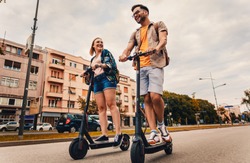 Young couple on vacation having fun driving electric scooter through the city.	