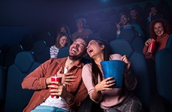 Group of cheerful people laughing while watching movie in cinema.