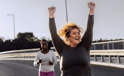Two excited young plus size women jogging together.