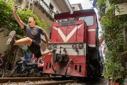 Man with mobile phone makes dangerously selfie photo in front of moving train. An undisciplined tourist in the popular Hanoi railway street, Vietnam.