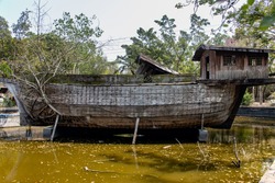 Abandoned ark in a dock in a water tank. The old wooden ship with roots of the tree grow from the side.