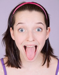 Girl sticking out her tongue. Cheerful girl poking out her tongue to the camera. Portrait of a Teenage girl pokes her tongue. Portrait of a beautiful girl showing her tongue. Young woman pokes tongue.