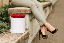 Image of woman's legs wearing black high heel shoes and checked trousers next to white box with red roses 