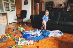 Adorable 1 year old baby boy with funny facial expression playing in a very messy living room