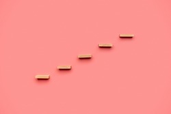Five wooden pegs placed over pink background to form a staircase.