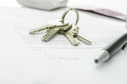House keys and money on a signed contract of house sale.  Focus on keys.