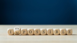 Word impossible spelled on wooden dices with the second one turning to spell the Its possible sign.