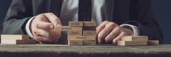 Businessman stacking wooden pegs with words of business strategy, vision and development on them in a conceptual image. 