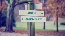 Rustic wooden sign in an autumn park with the words Simple - Complicated offering a choice of action and attitude with arrows pointing in opposite directions in a conceptual image.