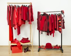 Wardrobe with red clothes hanging on a rack nicely arranged. Red clothes on hangers and accessories in a dressing room.