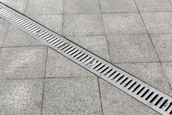 Trench drain gray with steel purification grate on granite stone tile road improvement of the city, close up details drainage system, nobody.