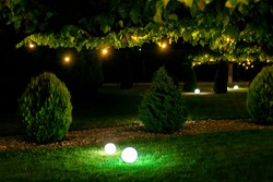illumination backyard light garden with electric ground sphere lantern with stone mulch and thuja bush in outdoor landscaping park with garland of warm light bulbs, dark illuminate night scene nobody.