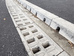 concrete grate drainage system for rain water drainage from asphalt road, highway with curb with storm water holes, close up road infrastructure, nobody.