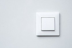 a light switch, a plastic mechanical switch of white color installed on a light gray wall.