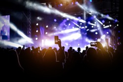 People with raised hands, silhouettes of concert crowd in front of bright stage lights
