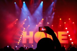 Hand with a smartphone records live music festival, Taking photo of rock concert stage, live concert, music festival. The word - hope - on stage, red light