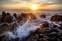 Golden waves of the ocean beat against the rocks, sunset