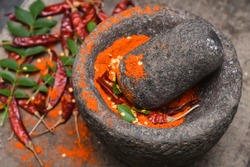 Dry red Kashmiri chilly/ chilli being crushed to powder in a traditional kitchen using vintage grinder / stone mortar, Kerala India. Indian spices for hot and spicy curry / cuisine / dish.