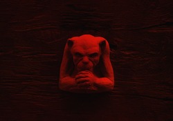 Stone carved gremlin figure on wood surface in red light
