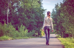 background girl standing turned her back on urban asphalt road  among trees and tall grass outside the town