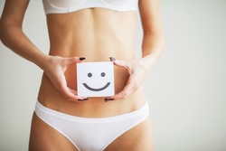 Women Health. Closeup Of Healthy Female With Beautiful Fit Slim Body In White Panties Holding White Card With Happy Smiley Face In Hands. Stomach Health And Good Digestion Concepts. High Resolution