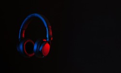 Black headphones lit with red and blue neon. Abstract minimal background. Copy space.