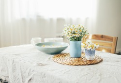 Table with flowers chamomile on linen tablecloth in living room, bright interior, Cottagecore Aesthetics