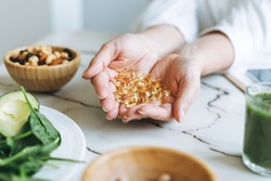 Woman doctor nutritionist hands in white shirt with omega 3, vitamin D capsules with green vegan food. The doctor prescribes a prescription for medicines and vitamins at clinic, healthy food