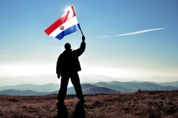 Successful silhouette man winner waving Paraguay flag on top of the mountain peak
