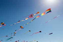 Sun flare and rays shine over colorful kites flying against a blue sky
