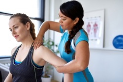Candid image of an attractive patient during a appointment with professional asian physiotherapist in design kinesio clinic working and massaging her neck and shoulder pain