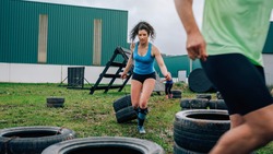 Female participant in an obstacle course dragging wheels seen from behind