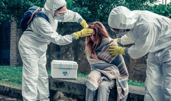 Doctors in bacteriological protection suits caring for a woman infected by a virus outdoors