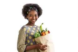 Young beautiful African black girl woman holding paper grocery shopping bag full of fresh healthy food, fruit and vegetable, on white background