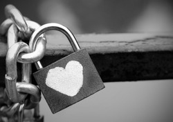 Love that cannot be broken, shown through a heart padlock chained to a fence, black and white.