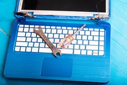 Wizard repairs laptop with tools and hands on the blue wooding table. top view. wrench and screwdriver on the keyboard. top view. Disassembly of the laptop into spare parts. View of the laptop inside