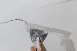 Worker fixing cracks on ceiling, spreading plaster using trowel