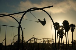As the sun sets a silhouetted man works out on gymnast rings