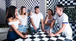 Group of positive adults standing near chessboard in quest room and solving conundrum