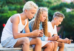 Modern concentrated kids spending time together outdoors using mobile gadgets