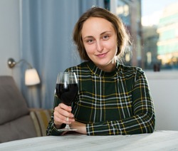 Portrait of young woman sitting at home with glass of wine