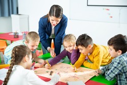 Young female teacher and happy schoolkids playing interesting board game during lesson in classroom